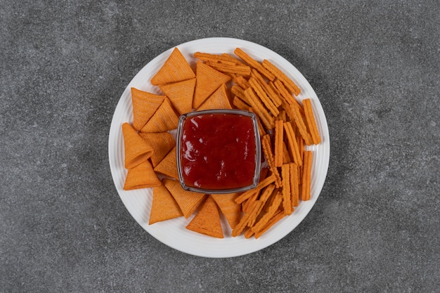 Ketchup, Corn Chips und getrocknetes Brot auf Teller auf der Marmoroberfläche