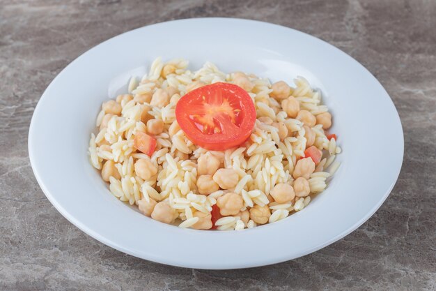 Kichererbsen und Nudeln mit Tomatenscheiben auf dem Teller, auf der Marmoroberfläche.