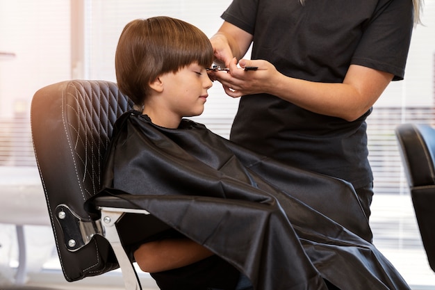 Kostenloses Foto kind bekommt haarschnitt bei seitenansicht des salons