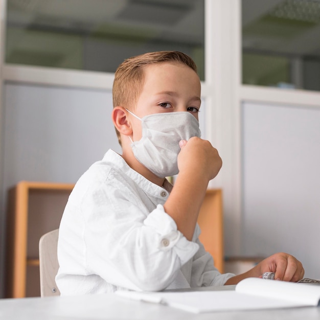 Kind, das eine medizinische Maske im Klassenzimmer trägt
