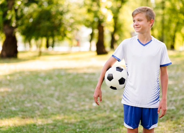 Kind, das einen Fußball draußen mit Kopienraum hält