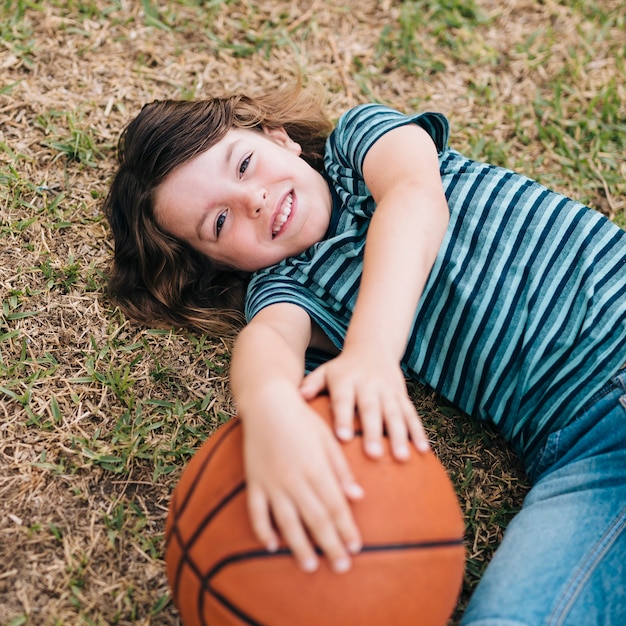 Kind, das im Gras liegt und Ball hält