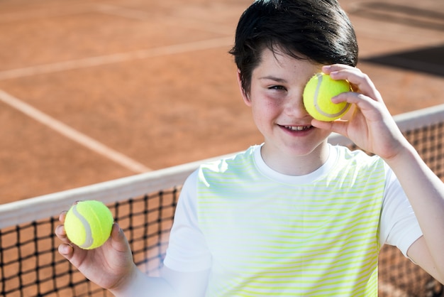 Kind, das sein Auge mit Tennisball bedeckt