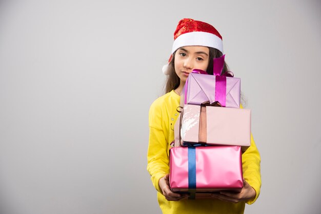 Kind gekleidet in den roten Hut des Weihnachtsmannes, der viele Weihnachtsgeschenke trägt. Hochwertiges Foto