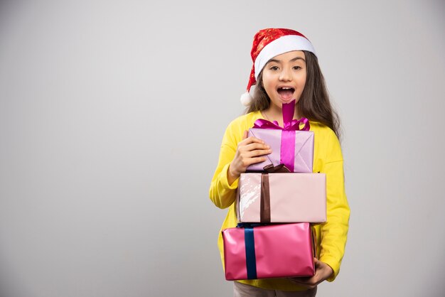 Kind gekleidet in den roten Hut des Weihnachtsmannes, der viele Weihnachtsgeschenke trägt. Hochwertiges Foto