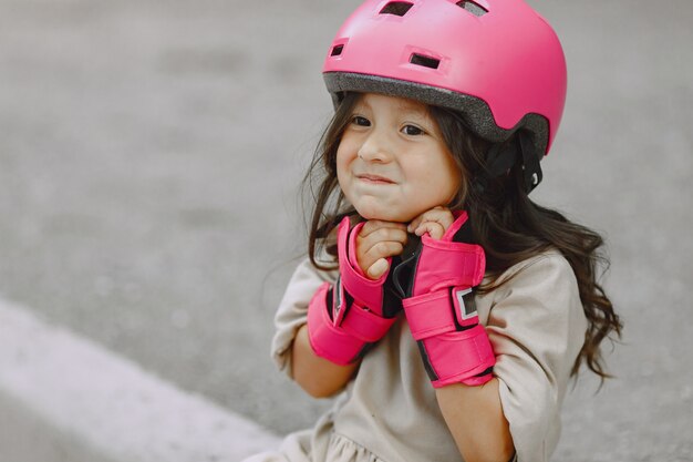 Kind in einem Sommerpark. Kind in einem rosa Helm. Kleines Mädchen mit einer Walze.