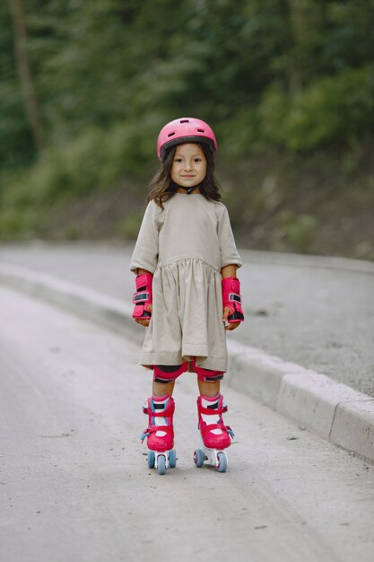 Kind in einem Sommerpark. Kind in einem rosa Helm. Kleines Mädchen mit einer Walze.