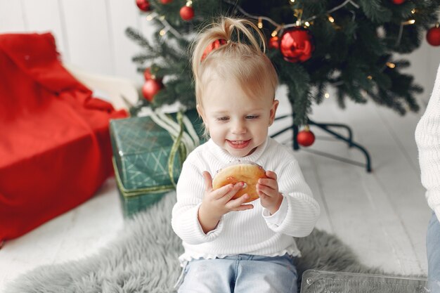 Kind in einem weißen Pullover spielt. Tochter steht in der Nähe von Weihnachtsbaum.