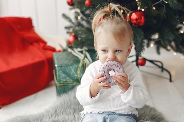 Kind in einem weißen Pullover spielt. Tochter steht in der Nähe von Weihnachtsbaum.