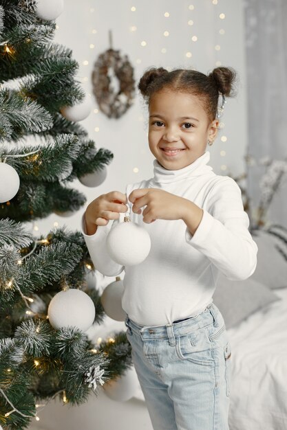 Kind in einem weißen Pullover. Tochter, die nahe Weihnachtsbaum steht.