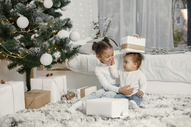 Kind in einem weißen Pullover. Töchter, die in der Nähe des Weihnachtsbaums stehen. Zwei Schwestern zu Hause.