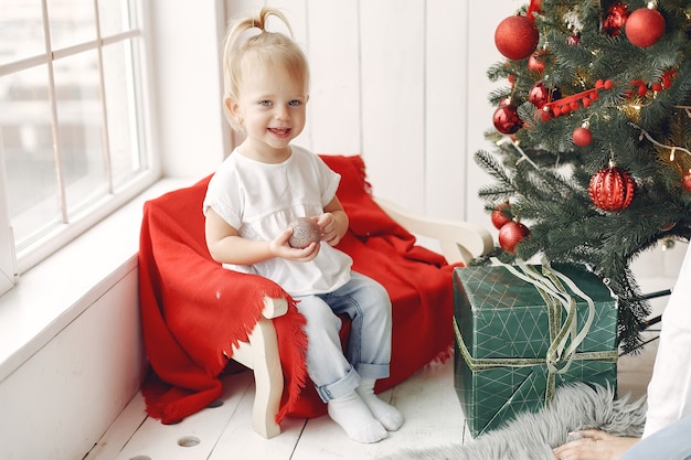Kind in einem weißen T-Shirt spielt. Tochter, die nahe Weihnachtsbaum sitzt.