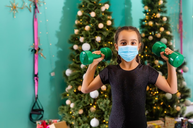 Kind in einer Weihnachtsmütze mit medizinischer Gesichtsmaske mit Weihnachtsgeschenkbox. Weihnachtseinkauf. Platz kopieren.