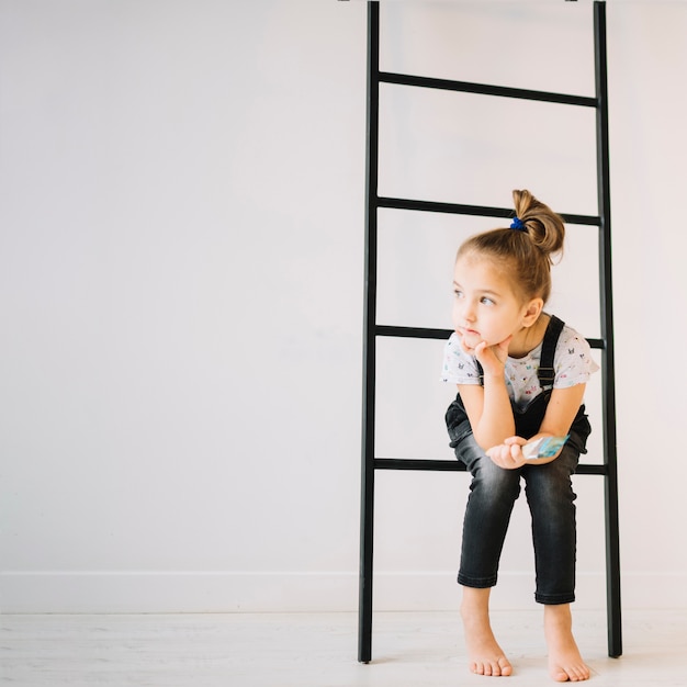 Kostenloses Foto kind mit der bürste, die auf leiter nahe wand im raum sitzt