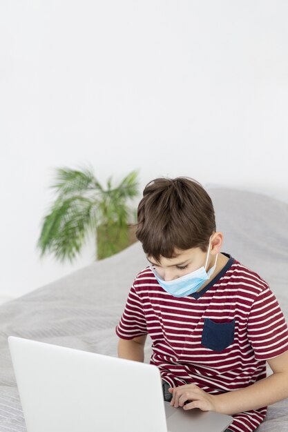 Kind mit der medizinischen Maske, die Laptop betrachtet