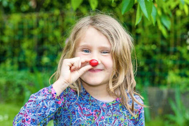 Kind mit Kirsche in der Hand in einem Garten