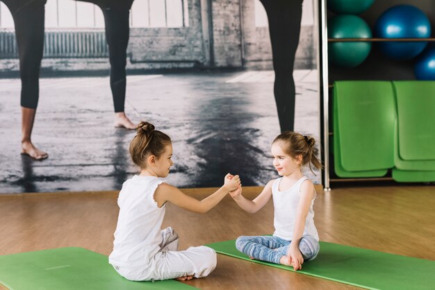 Kind mit zwei Mädchen, das auf Yogamatte sitzt und in der Turnhalle spielt