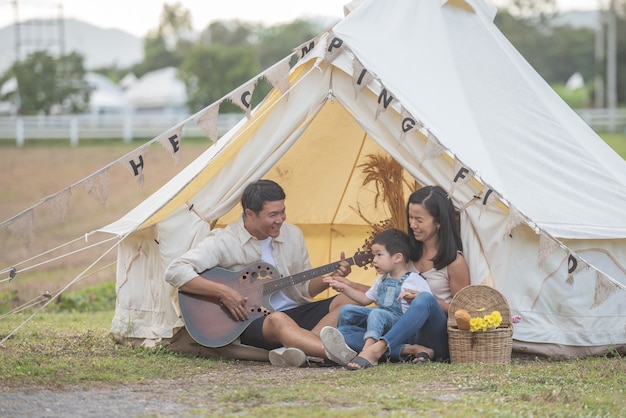 Kind singt mit lächelnder Familie auf dem Campingplatz. Familie, die Campingurlaub in der Landschaft genießt.