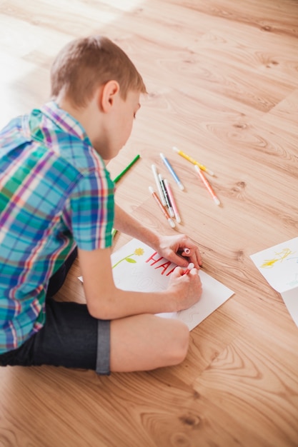 Kind sitzt auf dem Boden und Zeichnung für Muttertag