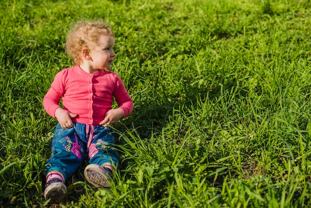 Kostenloses Foto kind sitzt auf gras und schaut zur seite