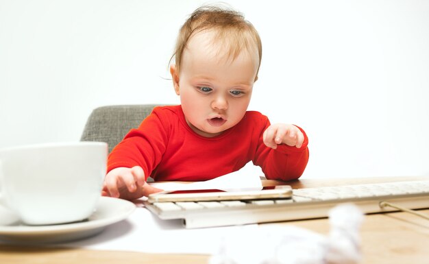 Kindbaby, das mit Tastatur des modernen Computers oder des Laptops im weißen Studio sitzt.