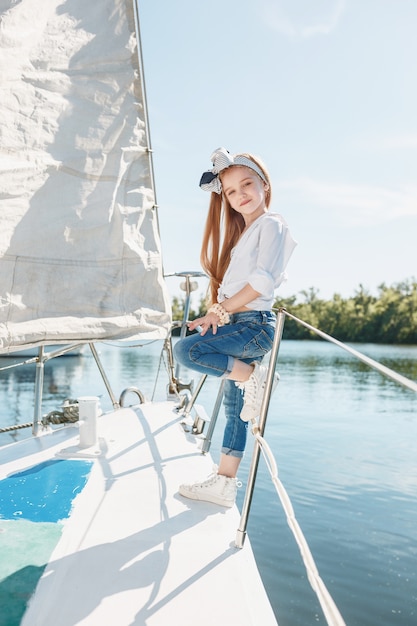 Kinder an Bord der Yacht trinken Orangensaft. Teenager- oder Kindermädchen gegen blauen Himmel im Freien. Farbenfrohe Kleider.