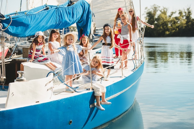 Kinder an Bord der Yacht trinken Orangensaft. Teenager- oder Kindermädchen gegen blauen Himmel im Freien. Farbenfrohe Kleider.