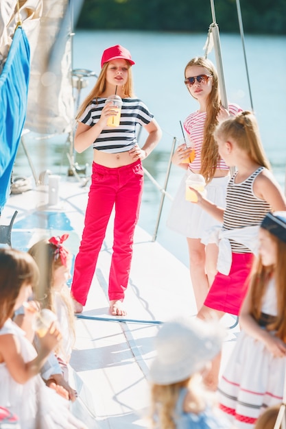 Kinder an Bord der Yacht trinken Orangensaft. Teenager- oder Kindermädchen gegen blauen Himmel im Freien