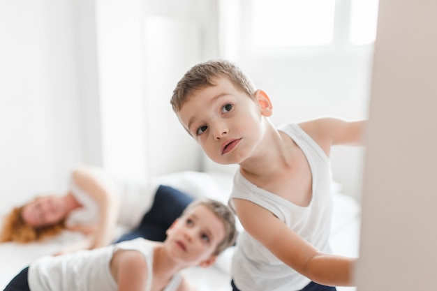 Kinder, die in Vordergrund nahe der Mutter schlafend auf Bett spähen