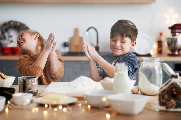 Kinder, die mit Mehl beim Backen von Keksen für Weihnachten umklammern