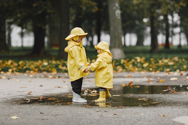 Kinder in einem Herbstpark. Kinder in gelben Regenmänteln. Leute, die Spaß im Freien haben.