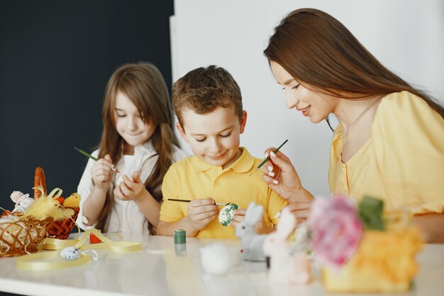 Kinder malen Eier. Mutter unterrichtet Kinder. An einem weißen Tisch sitzen.