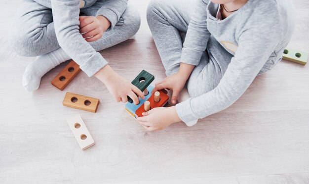 Kinder spielen mit einem Spielzeugdesigner auf dem Boden des Kinderzimmers. Zwei Kinder spielen mit bunten Blöcken. Kindergarten-Lernspiele