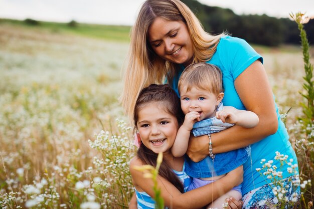 Kinder umarmen ihre Mutter, die auf dem Feld mit weißen Blumen steht