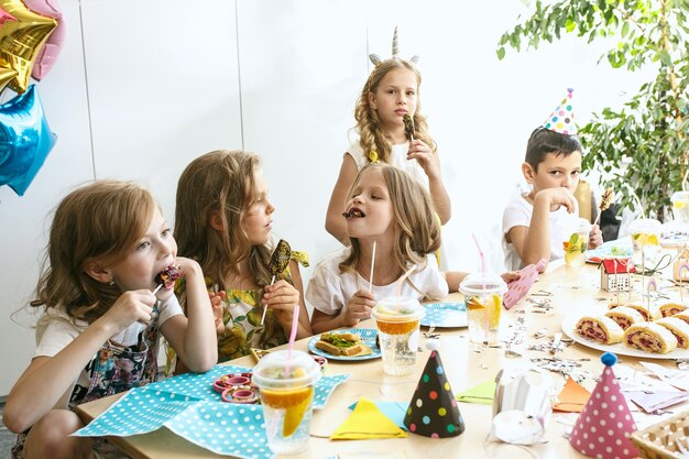 Kinder- und Geburtstagsdekorationen. Jungen und Mädchen am Tisch mit Essen, Kuchen, Getränken und Party-Gadgets.