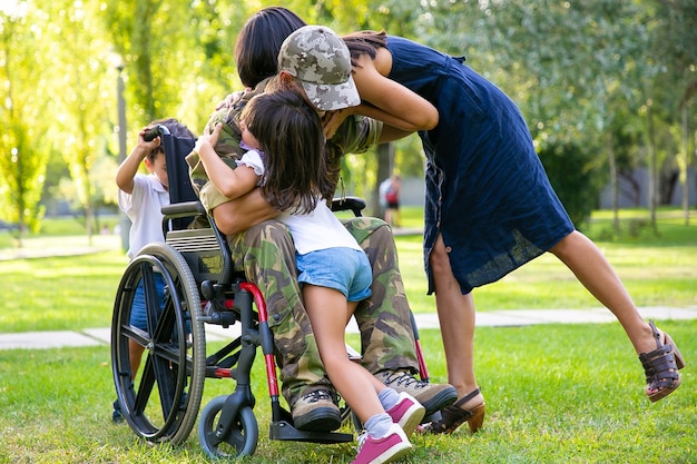 Kinder und ihre Mutter umarmen den behinderten Militärvater im Ruhestand im Park. Veteran des Krieges oder Rückkehr nach Hause Konzept