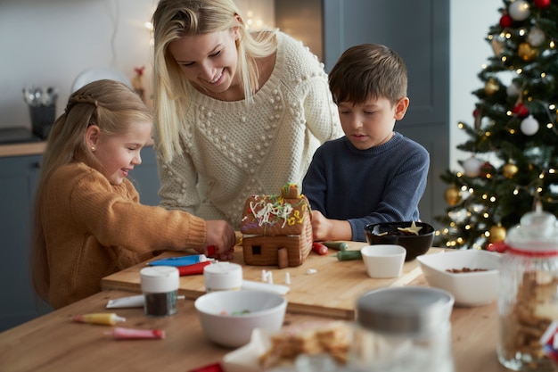 Kinder und Mutter verzieren Lebkuchenhaus in der Küche