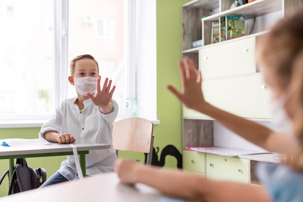 Kinder winken im Klassenzimmer und halten dabei soziale Distanz