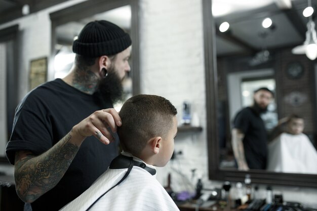 Kinderfriseur, der kleinen jungen gegen einen dunklen hintergrund schneidet.