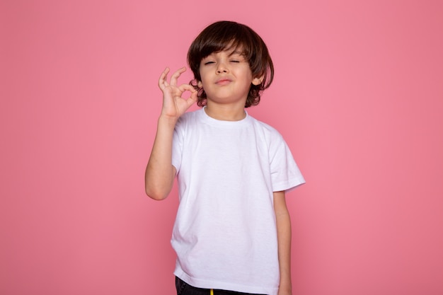 Kostenloses Foto kinderjunge, der zeichen entzückend niedlich auf rosa wand zeigt