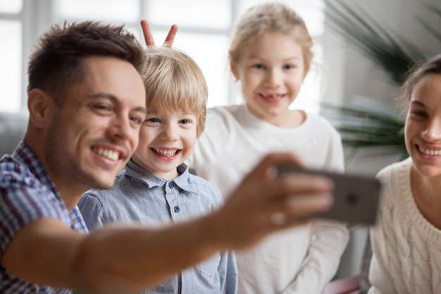 Kindermädchen, das Bruderhäschenohren während Vater nimmt selfie macht