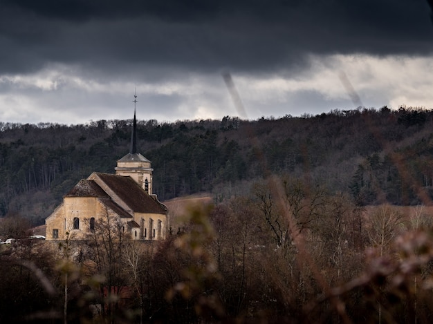 Kirche auf einem Hügel, umgeben von bewaldeten Hügeln unter einem bewölkten Himmel