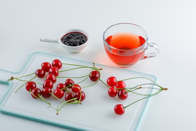 Kirsche mit Tee, Marmelade auf Weiß und Schneidebrett, hohe Winkelansicht.