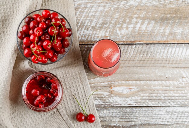 Kirschen in einer Schüssel mit Marmelade, Cocktail auf Holz und Küchentuch