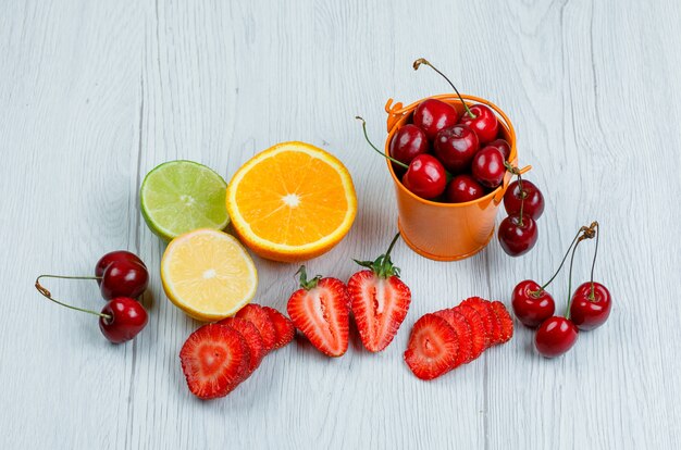 Kirschen mit Zitrone, Limette, Orange, Erdbeeren in einem Mini-Eimer auf Holztisch, flach liegen.