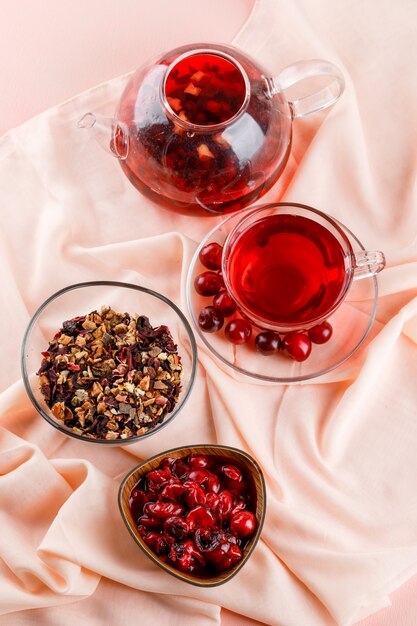 Kirschmarmelade mit Kirschen, Tee, getrockneten Kräutern in einer Schüssel auf Textil und Pink