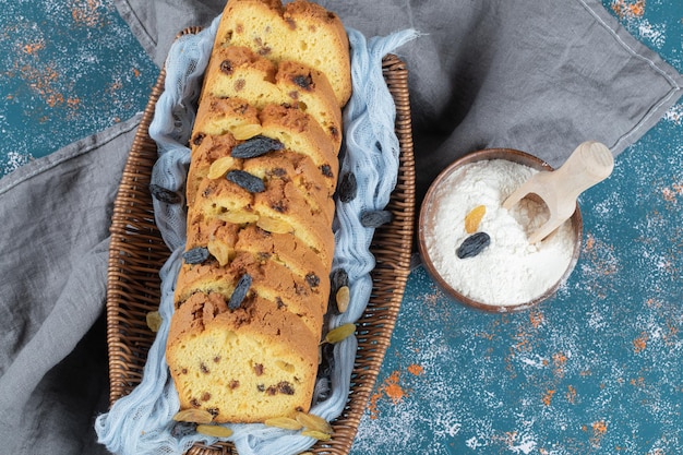 Klassische Sultaninenkuchenscheiben auf Holzkorb auf blauem Tuch.