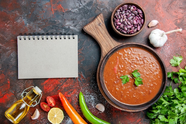 Klassische Tomatensuppe gefallene Ölflaschenbohnen und Notizbuch auf Schneidebrett auf einer gemischten Farbtabelle