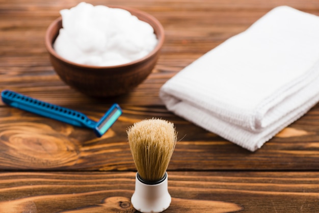 Kostenloses Foto klassischer rasierpinsel vor schaumstoffschale; gefaltete weiße serviette und rasiermesser auf hölzernem schreibtisch