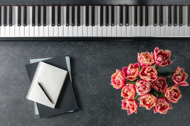 Klavierbucket mit Tulpenblumen und Notizbogen auf dunklem Hintergrund